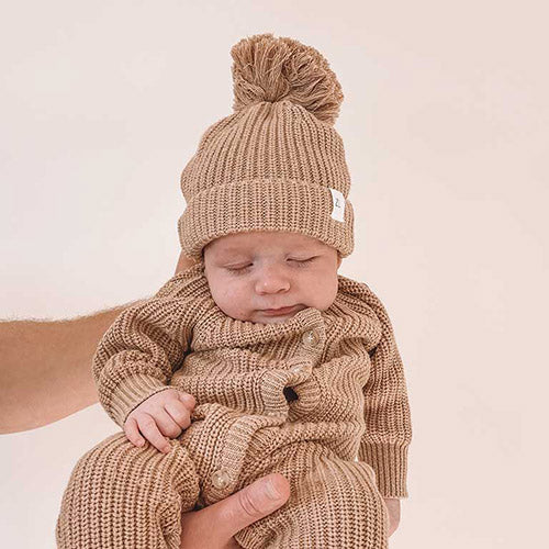 baby behind held by parent wearing fawn kintted beanie, booties and romper