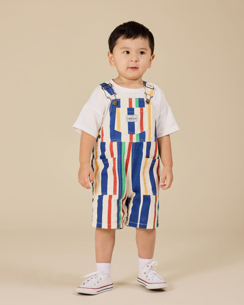 Child wearing a colorful striped overalls and white shirt on a beige background