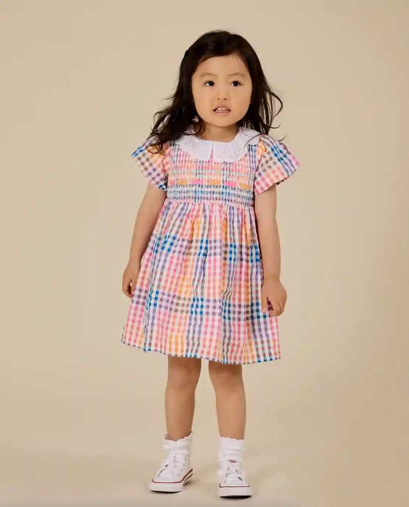 Young girl wearing a colorful checkered dress on a beige background