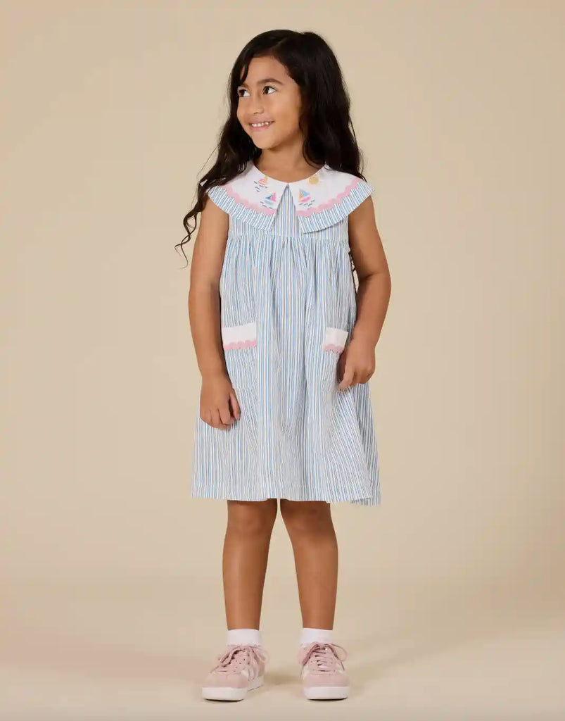 Young girl wearing a blue and white striped dress with pink accents on a beige background