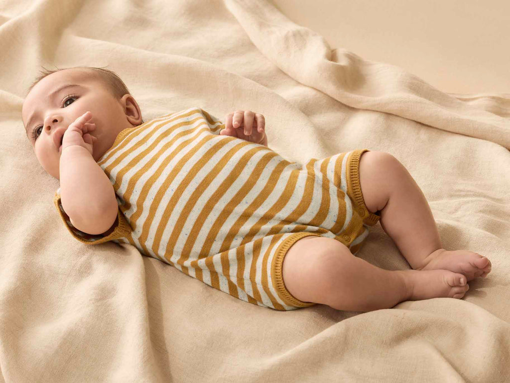 Baby in a mustard and white striped outfit lying on a beige blanket