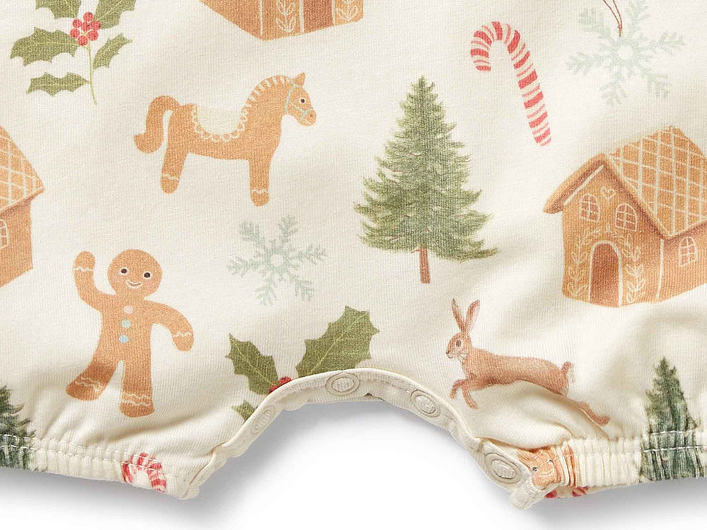 Close up of baby romper with Christmas-themed pattern including gingerbread men, trees, and houses on a white background.