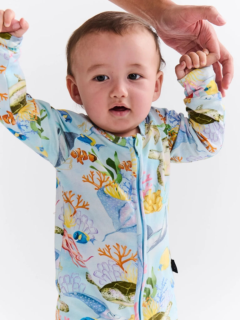 Baby wearing a colorful sea-themed onesie with hands held up.