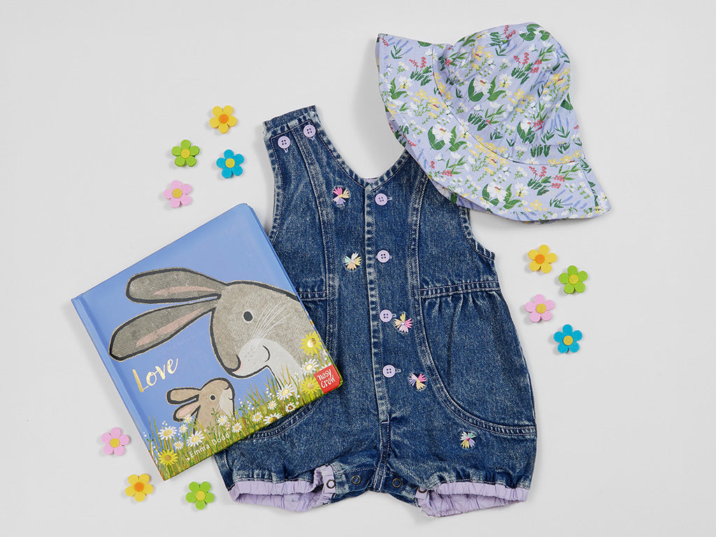 Children's denim romper with floral hat and book on a light gray background